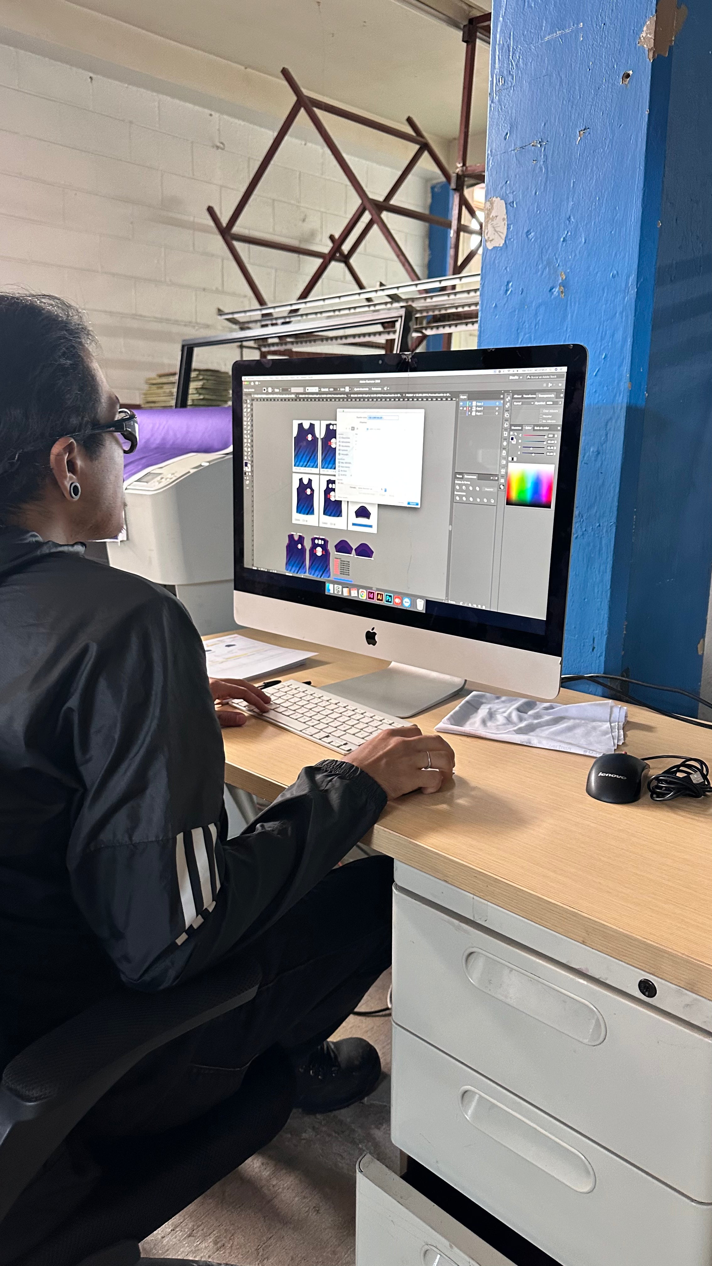 Diseñador trabajando en playeras sublimadas Dry Fit personalizadas con logotipos y gráficos a color.